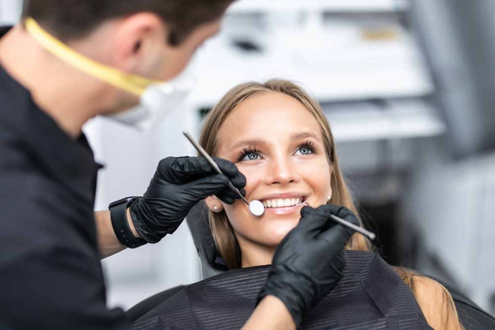 What Is a Prosthodontist in Knoxville?: a dentist examining a smiling young woman's teeth