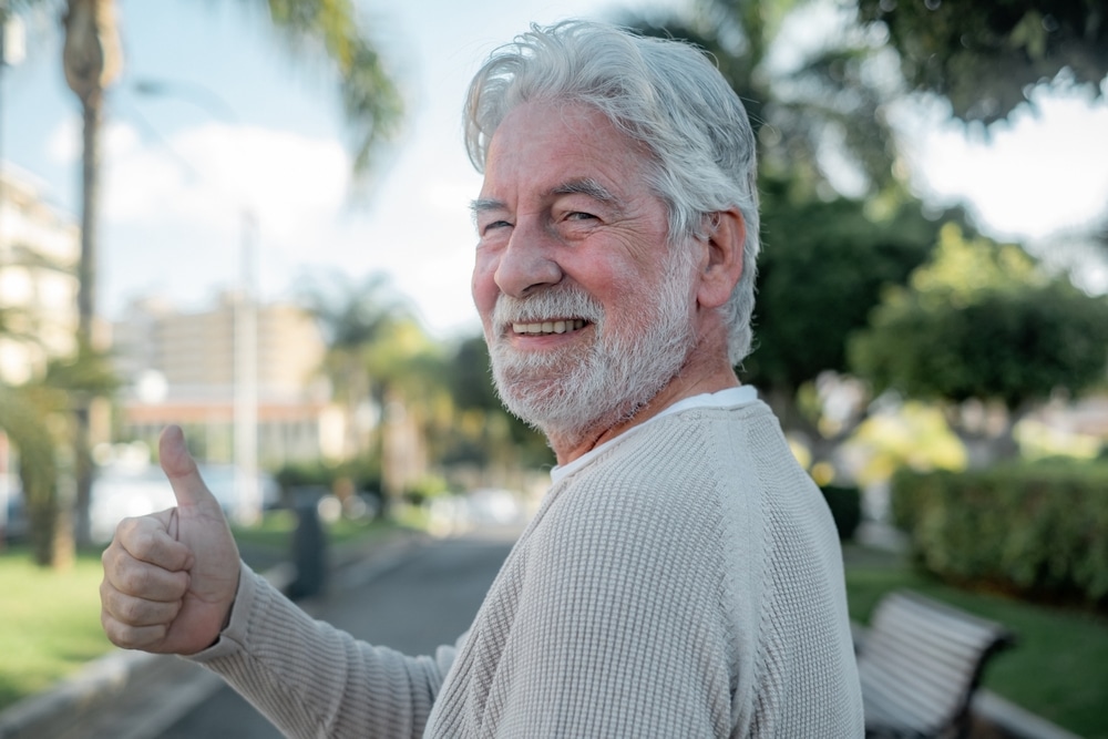 Hybrid Dentures Near Me: a smiling older man giving a thumbs-up outdoors